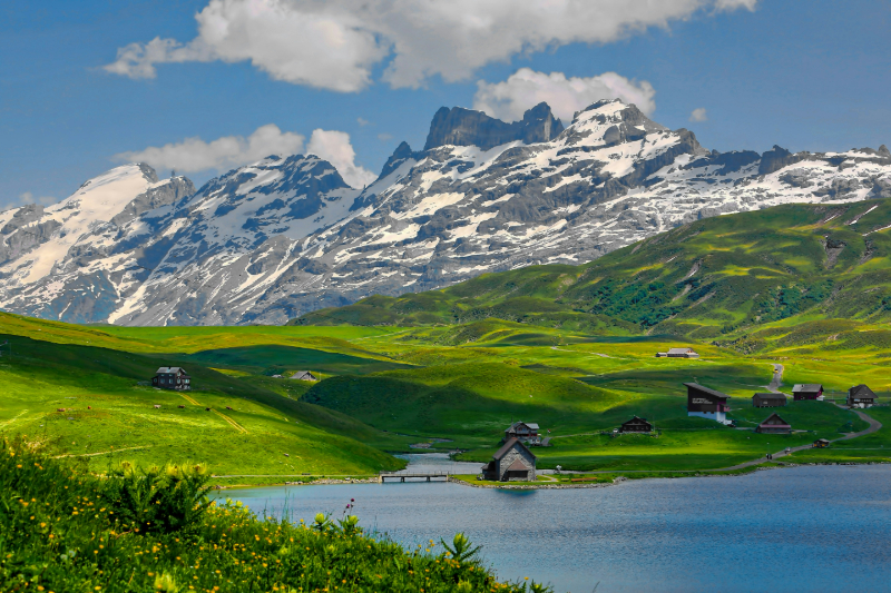 Sommerliche Berglandschaft mit Almhütten und See in den Schweizer Alpen.
